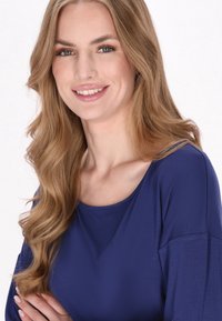 Sötétkék felső, széles kerek nyakkivágással és hosszú ujjal, sima, puha anyagból készült. Finom textúra, minimális dizájn részletek.