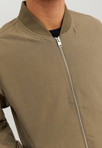 Khaki bomber jacket with a zip front, ribbed collar, and smooth texture. Features a fitted design and minimalistic style.
