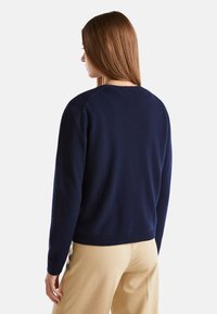 Granatowy sweter dzianinowy z długimi rękawami i okrągłym dekoltem, w luźnym fasonie, z prążkowanymi mankietami i dolnym obszyciem. Widoczna struktura.