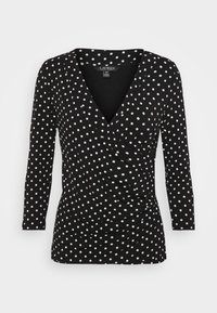 Musta pitkähihainen paita, jossa on kietaisusuunnittelu, valkoisia pilkkuja, V-mallinen pääntie ja ryppyinen rakenne vyötäröllä.
