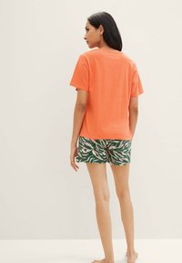 Orange Baumwoll-T-Shirt mit Rundhalsausschnitt, kombiniert mit grünen und rosa gemusterten Shorts mit einem zebraähnlichen Design.