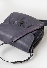 Borsa in pelle viola dal design morbido, con tracolla regolabile e texture sottile, dotata di chiusura nera e dettaglio del logo embossato.