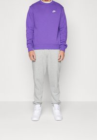Lila Nike sweatshirt, grå sweatpants och vita sneakers. Mjuk tyg, rund hals och logodetalj på sweatshirten. Avslappnad outfit.