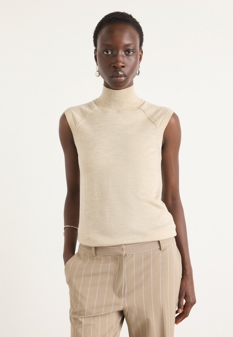Bež brezrokavni turtleneck top z oprijetim silhueto, narejen iz mehkega materiala, z diskretno teksturo in rebrastim ovratnikom.