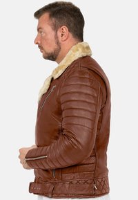 Giacca di pelle marrone con colletto in shearling sintetico, accenti trapuntati, design a righe sui gomiti e tasche con zip. La vista laterale mette in mostra la vestibilità e i dettagli.