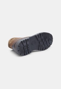 Brązowy zamszowy i skórzany but z ciemną gumową podeszwą. Posiada surowy wzór bieżnika oraz wzmocniony obcas dla lepszej przyczepności.