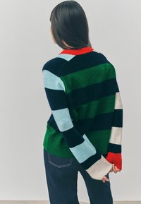 Gestreepte gebreide trui met groen, blauw, marineblauw en rode kleuren, voorzien van een geribbelde rode halslijn. De lange mouwen hebben verschillende strepen en een zachte textuur.