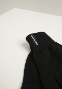 Black knitted fingerless gloves featuring a ribbed texture and a tag displaying "URBAN CLASSICS" on the cuff. Soft wool material.