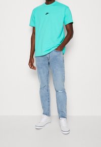 Turkos crew-neck t-shirt med svart Nike-logga, i kombination med ljusblå slitna jeans och vita sneakers. Avslappnad passform och standardtextur.