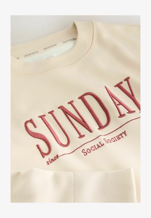 Beige sweatshirt met grote geborduurde "SUNDAY" in kastanjebruin, met daaronder de tekst "since" en "Social Society". Zachte textuur en geribde halslijn.