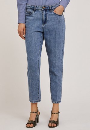 Jeans de mezclilla de color azul claro con un ajuste relajado, cintura alta, cinco bolsillos y un sutil efecto de desgaste. Combinados con sandalias de tacón negro con tiras.