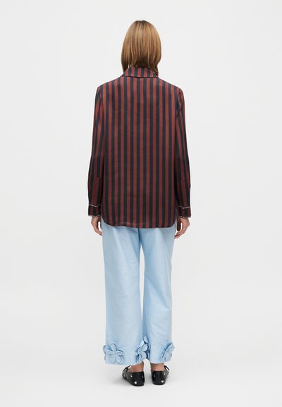 Bordó és fekete csíkos hosszú ujjú ing, világoskék nadrággal, amelynek szegélyén virágmintás díszítés található. Fekete cipő.