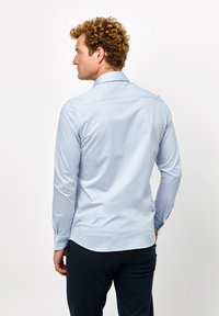 Lichtblauwe langemouwen overhemd met een button-down kraag, gladde stof en verstelbare manchetten, gezien vanuit de achterkant. Geen patronen of accenten zichtbaar.