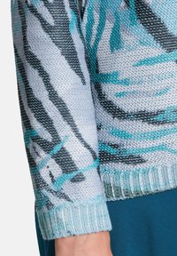 Stickad tröja med ett mönster av svarta och turkosa ränder på en ljusgrå bakgrund. Har en ribbad ärm i en ljusare nyans.