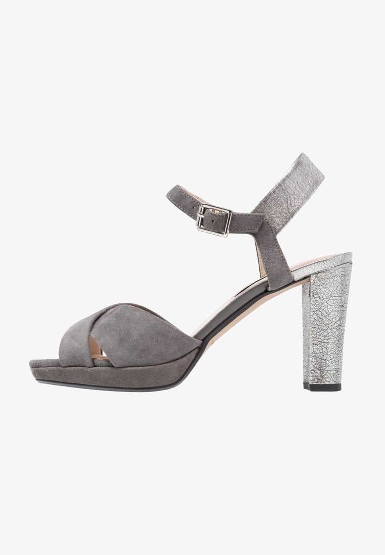 Sandale ouverte en suede gris avec une large sangle croisée et une sangle de cheville ajustable ; talon haut en métal argenté à texture craquelée.