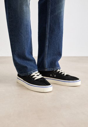 Mustad kanvas tossud valgete paeltega, siniste äärtega ja kummitaldadega, kantud tumedate teksadega, millel on sirge lõige ja kerge fading.