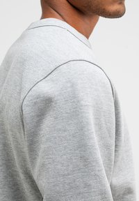 Grijze sweatshirt met een gladde textuur, ronde halslijn en subtiele naaddetails op de schouders. Eenvoudig en functioneel ontwerp.