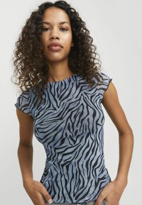 Top a maniche corte in tessuto blu con strisce zebrate nere, caratterizzato da un design aderente e bordi leggermente arricciati sulle maniche.