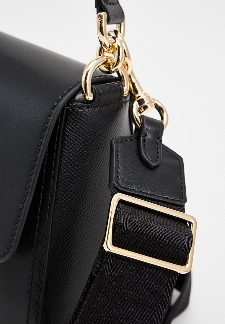 Sac à main en cuir noir avec une texture lisse, doté d'un fermoir en métal doré et d'une sangle en tissu réglable avec une boucle en métal carrée.