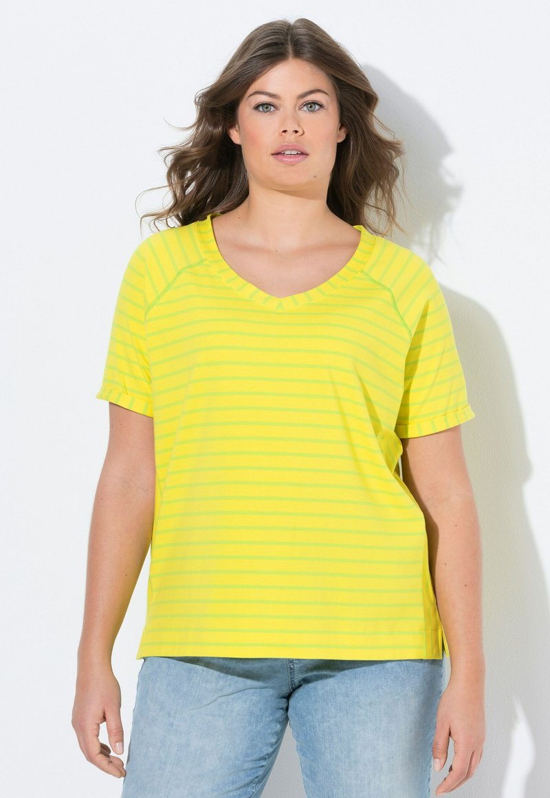 T-shirt jaune à rayures avec un col en V, des manches courtes et des poignets roulés. Fabriqué en tissu doux. Associé à un jean en denim bleu clair.