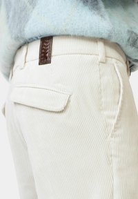Helle Cremefarbene Cordhosen mit vertikalen Rippungen. Ausgestattet mit einem dekorativen braunen Etikett am Bund und einer flachen Gesäßtasche.