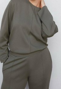 Set di abbigliamento da casa verde oliva composto da una maglia a maniche lunghe e pantaloni con vita elasticizzata. Realizzato in tessuto testurizzato con una vestibilità comoda.