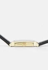 Montre rectangulaire en or avec un bracelet en cuir noir. Présente une petite couronne sur le côté et un cadran en verre affichant les indicateurs de temps.
