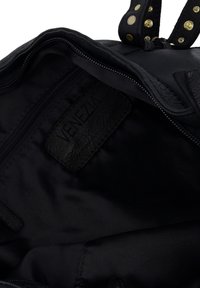 Vnitřek černé kožené kabelky s textilním podšívkou. Obsahuje zipovou kapsu a šitý kožený štítek s nápisem "Venezia." Viditelné zlaté kovové detaily.