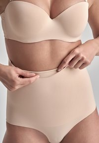 Slip modellante beige a vita alta, senza cuciture, realizzato in un tessuto morbido, con un pannello di controllo mirato e bordi lisci.
