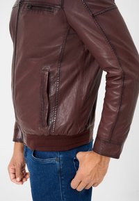 Burgundy läderjacka med en zippered ficka, ribbade manschetter och nederkant, samt en elegant design. Bärs över blå denimjeans.