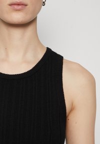 Μαύρη ριμπ αμάνικη μπλούζα με στρογγυλή λαιμόκοψη. Το ύφασμα φαίνεται μαλακό με κάθετες γραμμές και εφαρμοστή σιλουέτα.