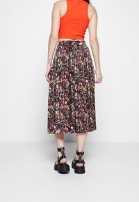 Blomster midi nederdel med smock liv, der har en sort bund med farverige blomstermønstre; parret med kraftige sorte sandaler.