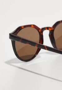 Óculos de sol octagonais com tonalidade castanha e padrão de tartaruga. Armações grossas com detalhes pretos. As hastes elegantes melhoram o design angular.