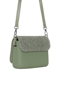 Borsa verde con un patta tessuta e strutturata e corpo in pelle liscia. Cinturino regolabile e dettagli in metallo. Forma compatta e rettangolare.