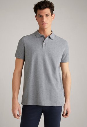 Man wearing a light grey short-sleeve polo shirt and dark pants standing against a plain light background.