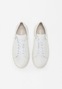 Valkoiset nahka-adidas-kengät, joissa on litteät valkoiset nauhat, pyöreä kärki ja kermavärinen pohja. Sisäpuolella on "Best Fitting" ja "Gab" -brändäys.