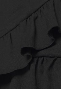 Tissu noir avec une surface texturée, présentant des accents froncés le long des bords. Le matériau est léger et légèrement transparent.