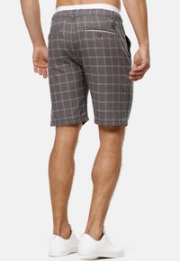 Shorts à carreaux gris en tissu texturé, avec des poches latérales et une poche arrière avec des boutons. Portés avec des baskets blanches.