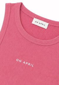 Haut sans manches côtelé rose avec encolure ronde et texte blanc "OH APRIL" imprimé sur la poitrine et sur l'étiquette intérieure.