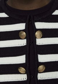 Cardigan a righe in maglia blu navy e bianca, con bottoni dorati e un tessuto testurizzato, dotato di un classico scollo rotondo.