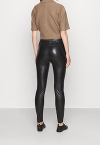 Svarta läderleggings med en slät, glänsande yta, kombinerat med en kort, åtsittande brun topp. Utsikten visar baksidan och sidan av outfiten.