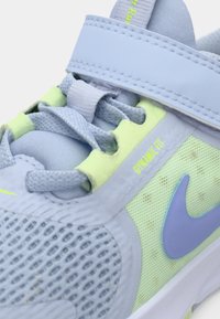 Světle modrá sportovní bota s pletivovým svrškem, neonově zelenými akcenty a fialovým logem Nike. Obsahuje nastavitelné zapínání a texturované povrchy.