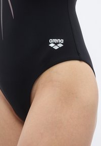 Μαύρο ολόσωμο μαγιό με ομαλή υφή. Διαθέτει λευκό λογότυπο «arena» και μινιμαλιστικό σχεδιασμό. Ψηλές ανοίγματα στα πόδια.