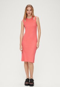 Dopasowana, bezrękawnikowa sukienka midi w jasnym koralowym kolorze z prążkowanej tkaniny, z bocznymi rozcięciami i gładką fakturą. Noszona z masywnymi czarnymi sandałami na platformie.