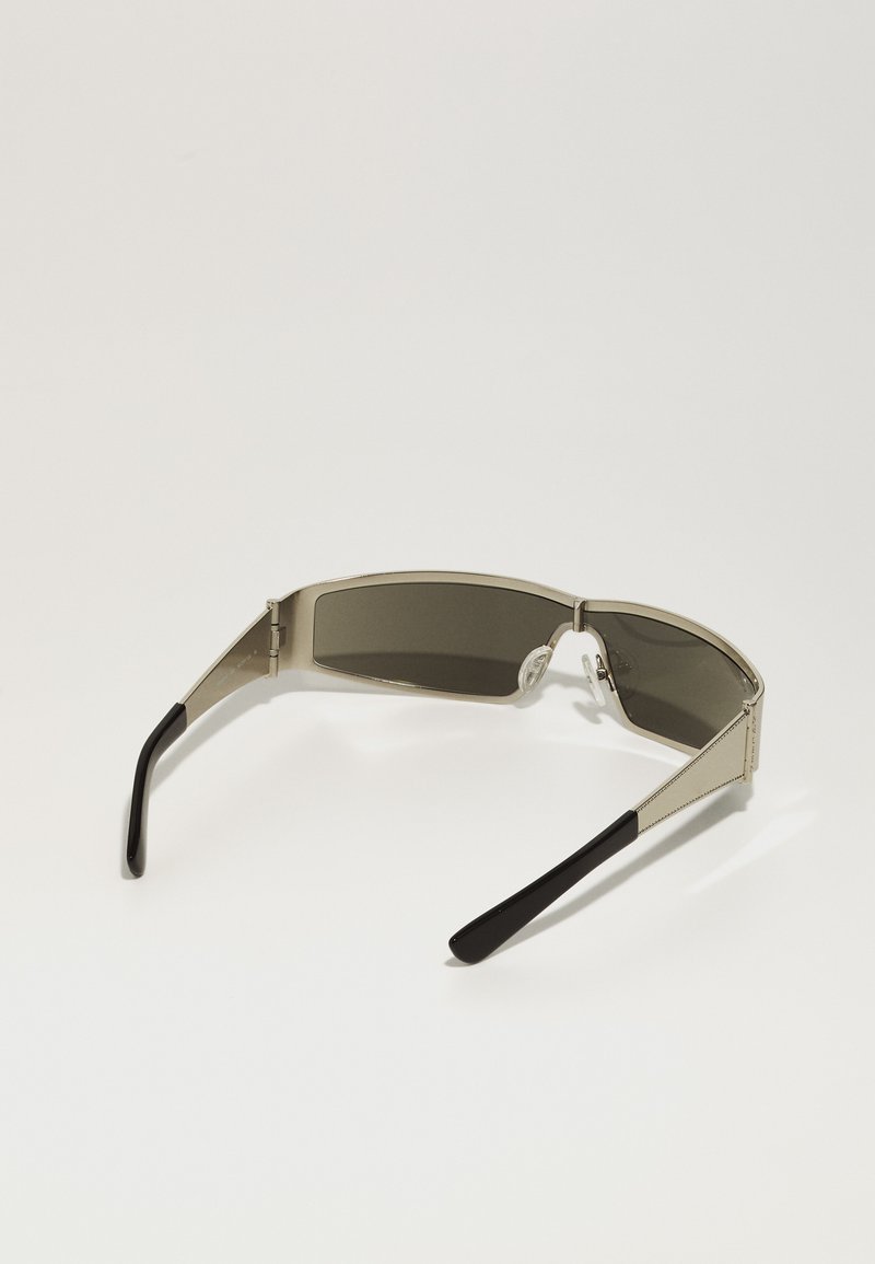 Sonnenbrille mit einem silbernen Metallrahmen und grauen, getönten Gläsern. Schwarze Kunststoff-Enden und eine geometrische Linsenform. Verfügt über Nasenpolster für zusätzlichen Komfort.