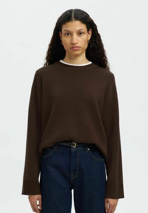 Pull en tricot marron avec un col rond, des manches longues, des poignets côtelés et une coupe décontractée, associé à un jean bleu foncé et une ceinture noire.