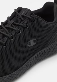 Svart idrottssko med strukturerad mesh-ovandel, rund tå, snördesign och dämpad gummisul med mönstrad yta.