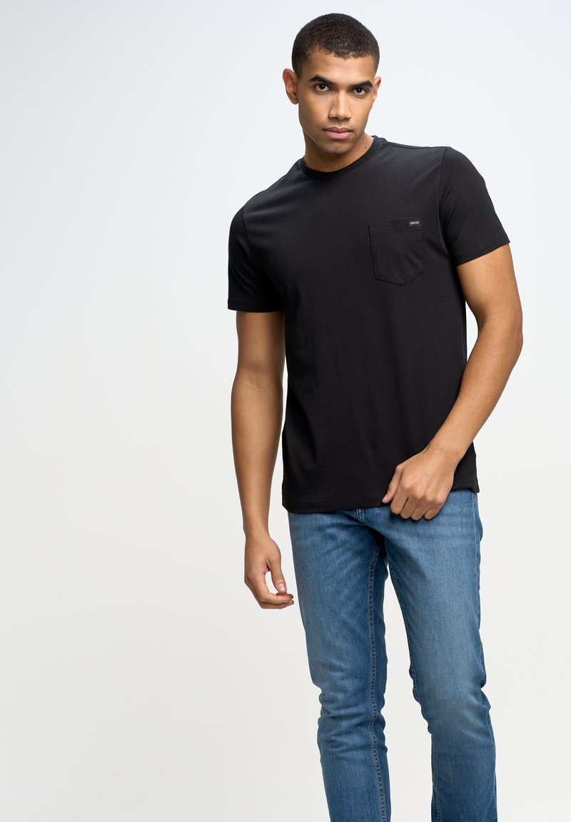 Černé krátké tričko z bavlny s kapsou na prsou. Nosit s modrými džínami, ukazuje volný střih a minimalistický design.