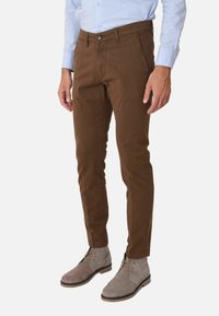 Pantaloni in cotone marroni con vestibilità slim, dotati di chiusura con bottone e tasche laterali, abbinati a stivaletti alla caviglia in suede grigio.