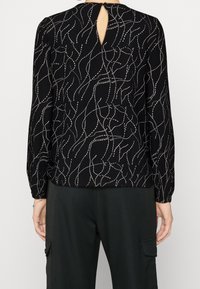 Sort bluse med lange ærmer, der har en nøglehulsvendebag, udsmykket med hvide svungne linjer og prikker, tekstureret stof med let gennemsigtighed.